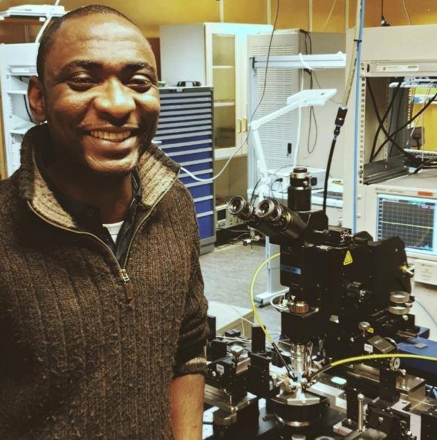 Temitope Odedeyi smiling beside an on-wafer probe station in a microwave laboratory