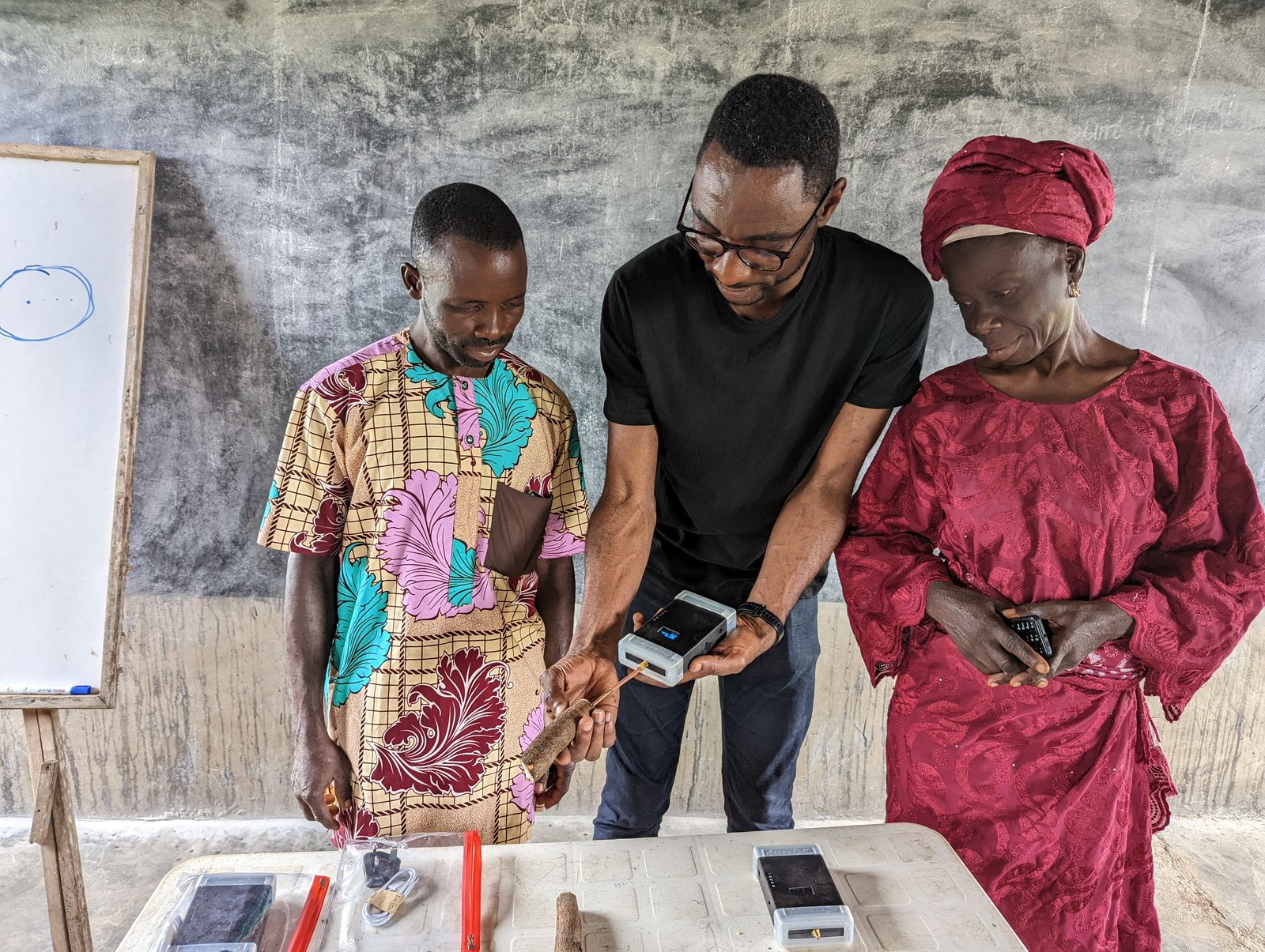 Temitope Odedeyi showing two farmers how to take a reading from a cassava root with a handheld sensor and probe